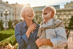 senior couple laughing while standing in the park together on a sunny day