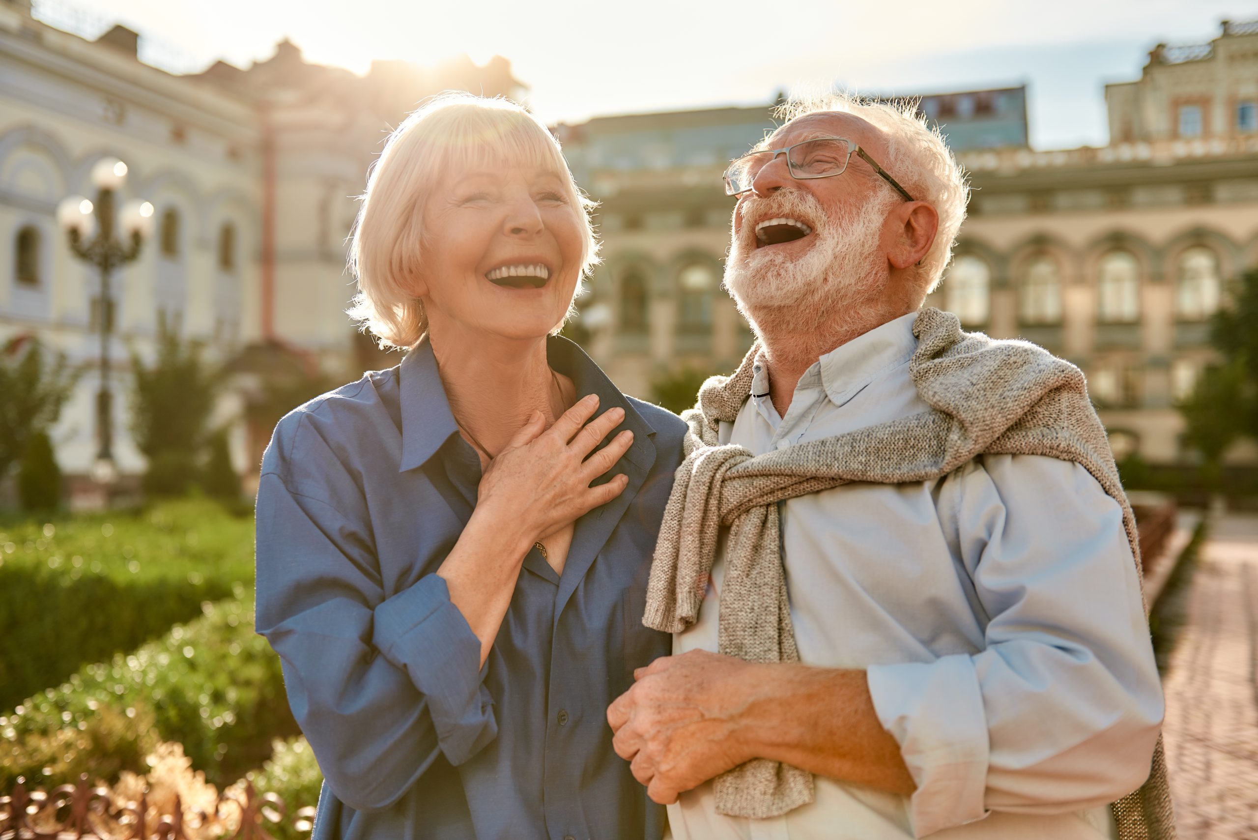 senior couple laughing while standing in the park together on a sunny day