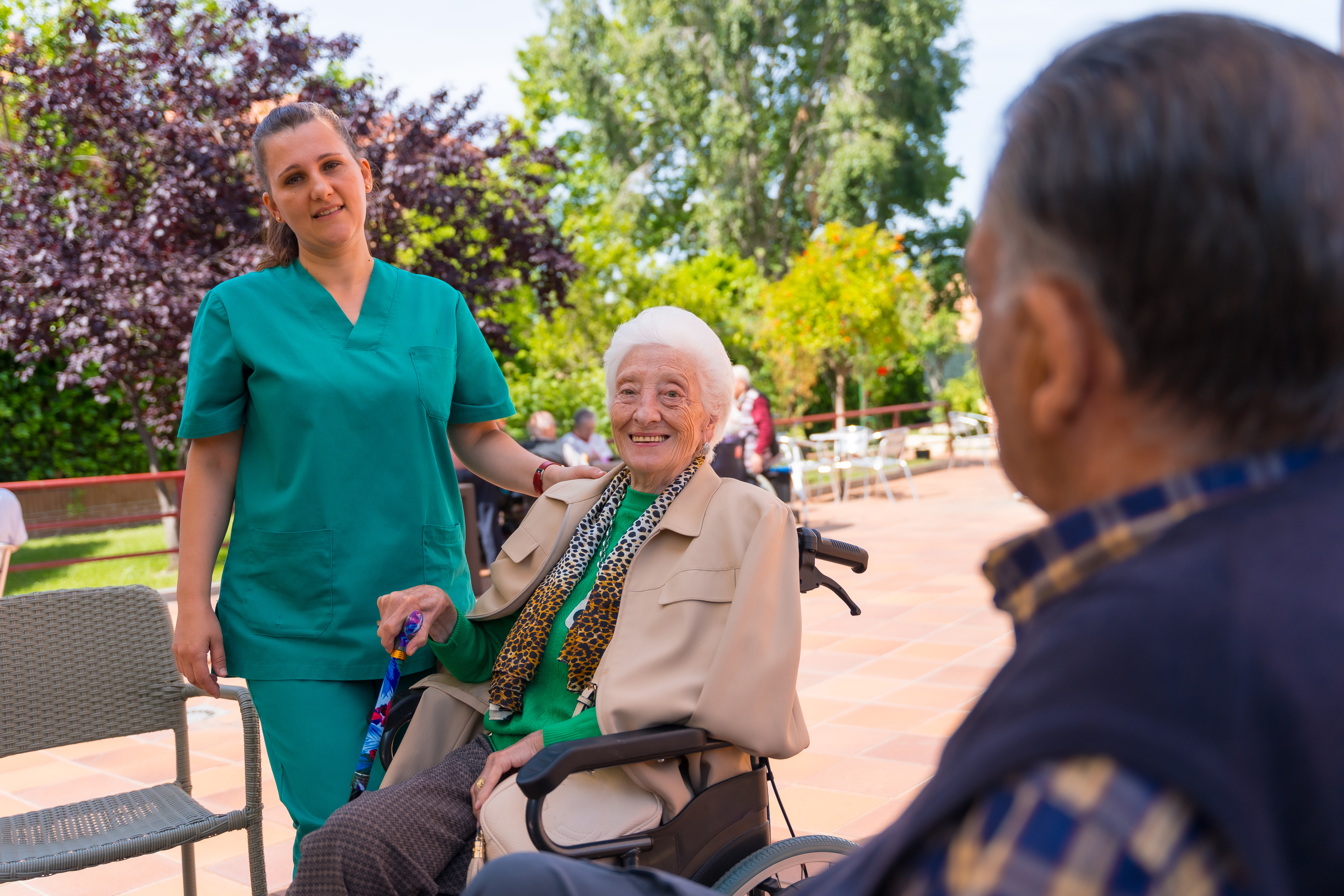 Portrait of an elderly woman in a wheelchair with a nurse in the garden of a nursing home